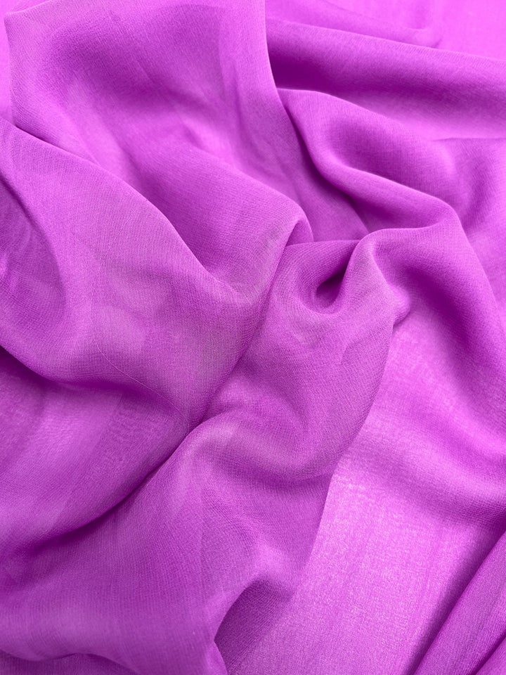 A close-up view of the sheer Silk Georgette - Iris from Super Cheap Fabrics, in vibrant purple. The lightweight 135cm fabric appears slightly translucent, with soft folds and gentle curves creating intricate patterns and textures, perfect for spring and summer outfits.