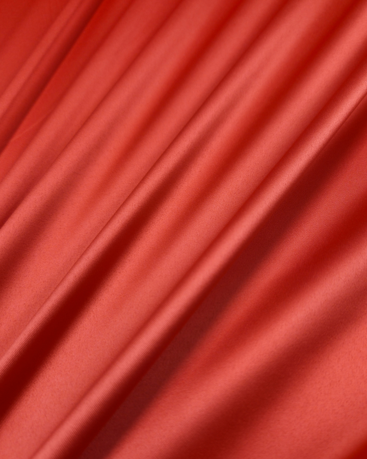 A close-up of the Satin Deluxe fabric in Grenadine, available in 150cm width by Super Cheap Fabrics, reveals a smooth, flowing texture with gentle diagonal folds and a shiny finish, exuding elegance.
