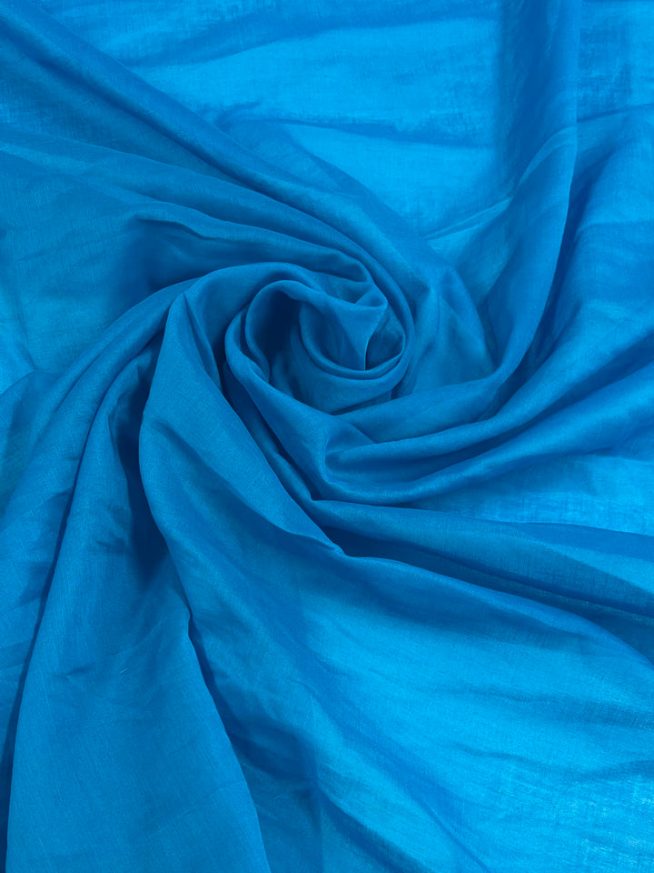 A close-up of Super Cheap Fabrics' Cotton Voile - Vivid Blue - 135cm, 100% cotton fabric swirled into a spiral pattern. The texture of the material appears smooth and silky, with soft folds and gentle shadows enhancing the rich, bold color.