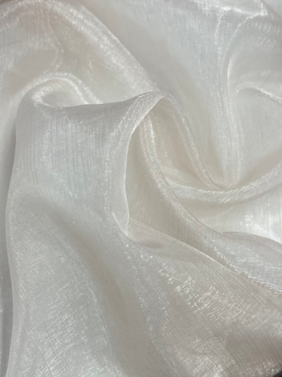 The image shows a close-up of the Organza - Pearl - 150cm fabric by Super Cheap Fabrics, featuring delicate folds and a subtle shimmer that highlights its sheer and airy texture.