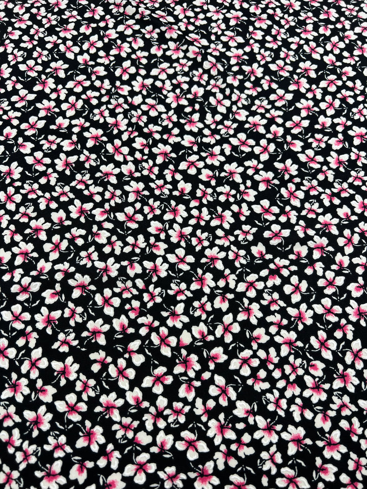 A close-up view of black medium weight fabric with a dense pattern of small white flowers, each adorned with a pink center. This Super Cheap Fabrics' Printed Lycra - Moonwalk - 150cm's repetitive floral design gives it a vibrant and detailed appearance, making it perfect for children's clothing.