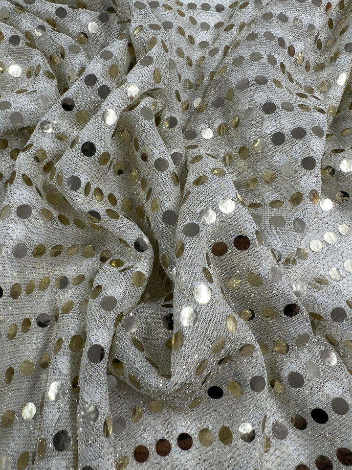 The Sequin - White Gold - 112cm fabric by Super Cheap Fabrics features a metallic silver base embellished with shiny gold and silver polka dots, making it ideal for dancewear. Its crumpled and draped folds produce a textured, reflective surface that catches the eye with its brilliant shine.