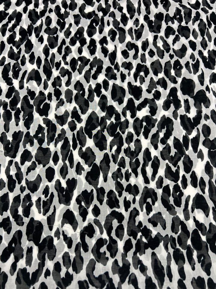 Introducing the Pure Printed Silk Voile - Snow Leopard - 145cm by Super Cheap Fabrics. This exquisite piece features a black and white leopard print pattern on a white background, adorned with irregularly shaped black spots that create a coarse yet consistent texture. Ideal for dresses, its extra light weight ensures both comfort and elegance.