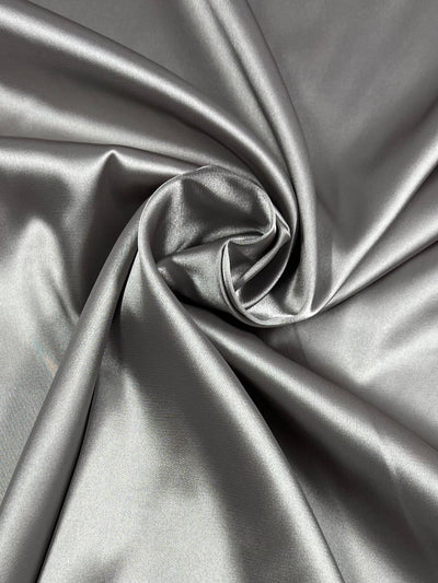 A close-up image of smooth, shiny Super Cheap Fabrics Satin Deluxe - Clouds - 150cm gathered in a gentle swirl. The surface, with its shiny finish, reflects light beautifully, highlighting the silky texture and creating a sense of flowing motion in this lightweight fabric.