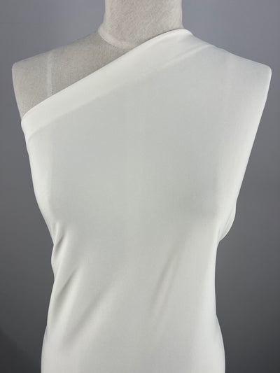 An ivory, one-shoulder dress displayed on a mannequin against a plain gray background. Made from Double Knit Jersey - Ivory by Super Cheap Fabrics, the medium-weight polyester spandex blend drapes elegantly over the form, showcasing its smooth, sleek appearance and minimalist modern design.