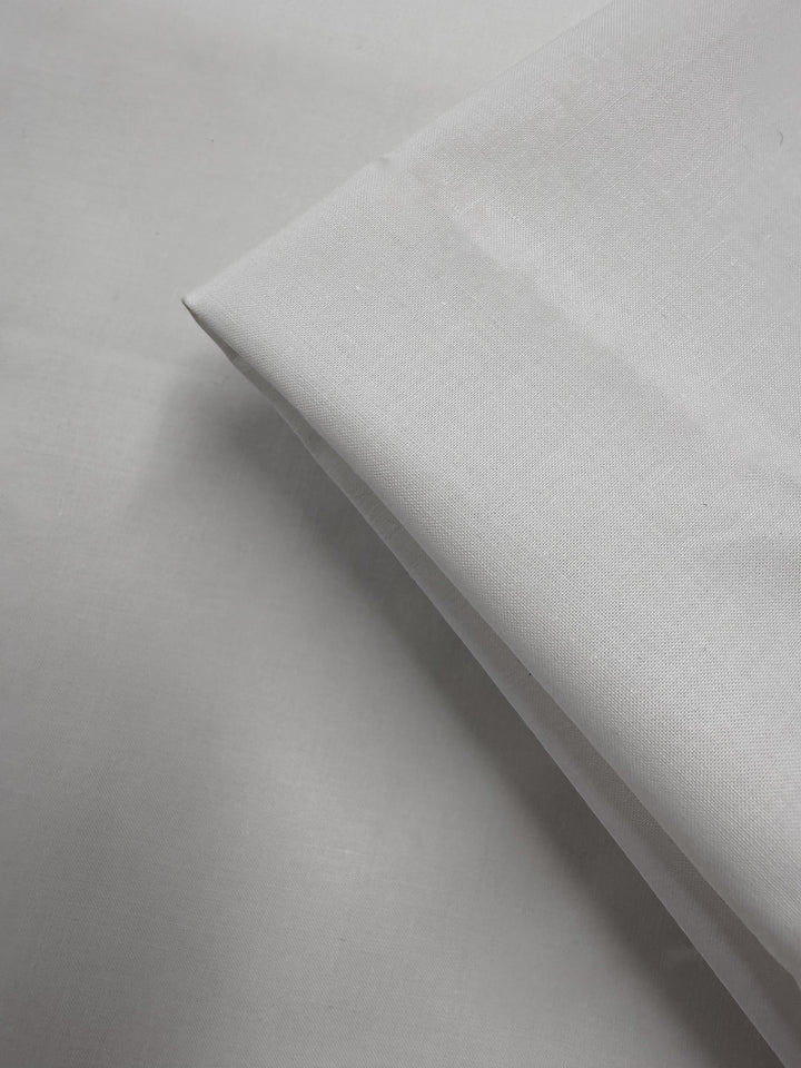A close-up of Super Cheap Fabrics' Cotton Voile - Gardenia (150cm), neatly folded on a white surface, highlights its smooth texture and sharp edges.