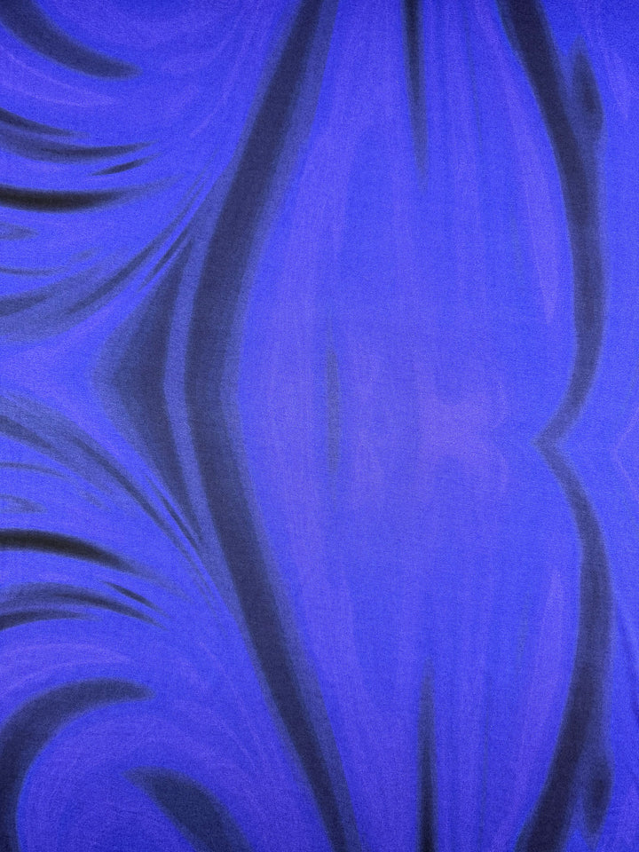 The Viscose Knit - Ocean Blur - 140cm from Super Cheap Fabrics features swirling blue and black waves, creating a dynamic, textured look inspired by stretch knit fabric with a striking central vertical wave pattern.