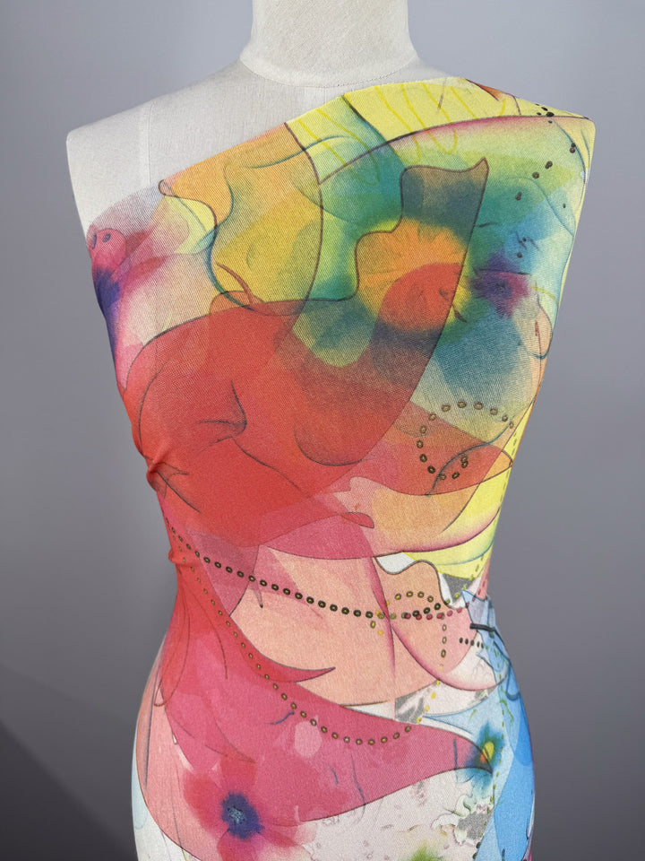 A close-up showing Super Cheap Fabrics’ Viscose Knit - Watercolour Bloom (142cm) on a mannequin, featuring an abstract floral pattern in red, yellow, green, and blue with dotted accents on breathable summer fabric.