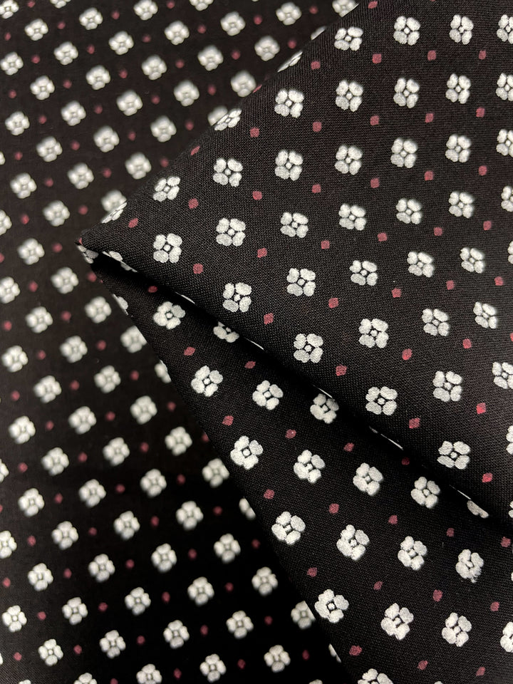 Close-up view of Super Cheap Fabrics' Linen Voile - Reap, featuring a black base adorned with small white flowers and tiny pink dots. The lightweight fabric is folded to showcase its repeating geometric design, making it ideal for home decor projects. Width: 145cm.