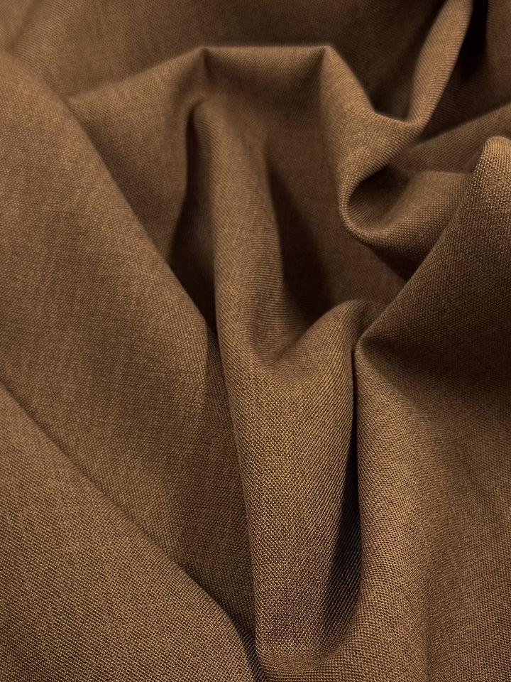 A detailed view of Twill Suiting - Raw Hide (150cm) by Super Cheap Fabrics shows its brown polyester with a soft texture and visible diagonal weave, gently gathered in folds.
