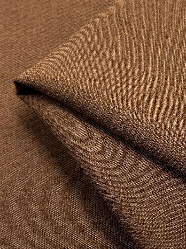 A close-up of Twill Suiting - Raw Hide - 150cm by Super Cheap Fabrics displays its brown folded fabric with a fine diagonal weave, clean sharp edges, and soft shadows.