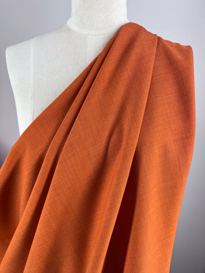 A white mannequin is styled with "Twill Suiting - Rust - 150cm" polyester from Super Cheap Fabrics, draped over one shoulder in a diagonal weave, set against a plain light gray background.