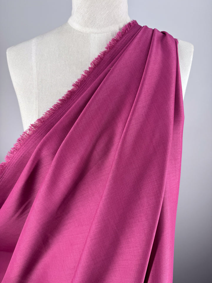 A mannequin displays Super Cheap Fabrics' Twill Suiting in Fuchsia Rose (150cm), a bright magenta polyester with a frayed edge and subtle diagonal weave, set against a plain light gray background.