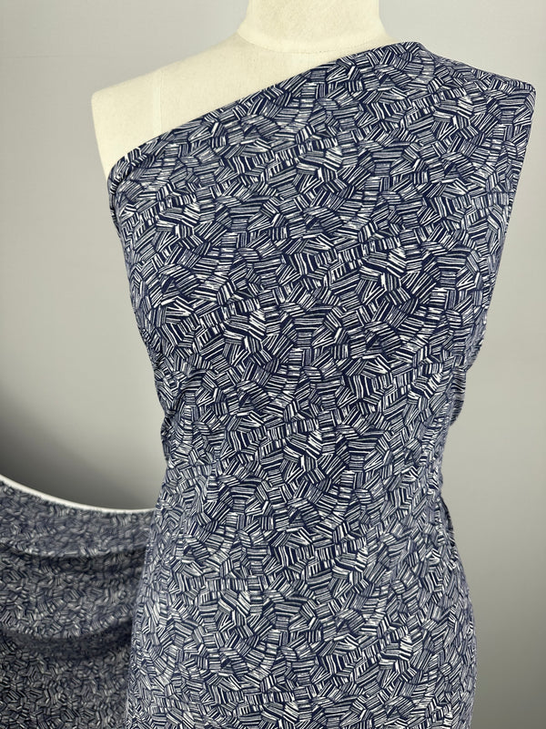 A mannequin is draped in medium-weight, dark blue and white Printed Lycra - Mosaic Stripe from Super Cheap Fabrics, featuring a geometric leaf pattern. The fabric elegantly covers one shoulder of the mannequin, while another piece of the same Polyester/Spandex fabric can be seen in the background.