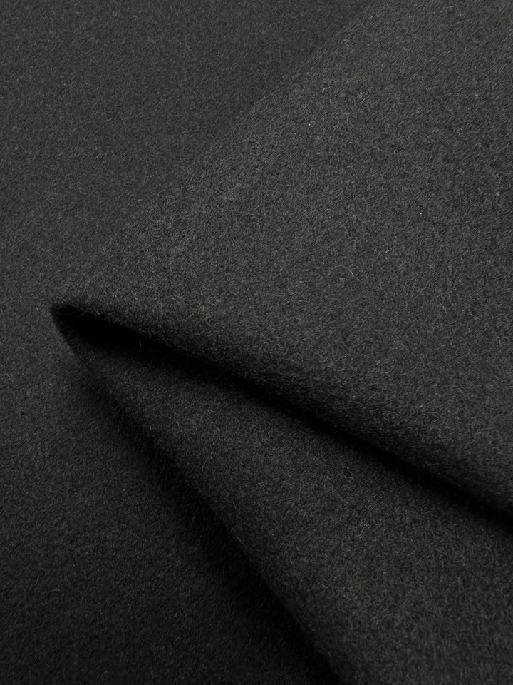 A close-up of the Wool Flannel - Black - 150cm fabric from Super Cheap Fabrics, highlighting its smooth yet slightly textured surface. The detailed shot showcases its thickness and soft texture, with the folds forming sharp angles that emphasize the heavy-weight wool material's structure and drape.