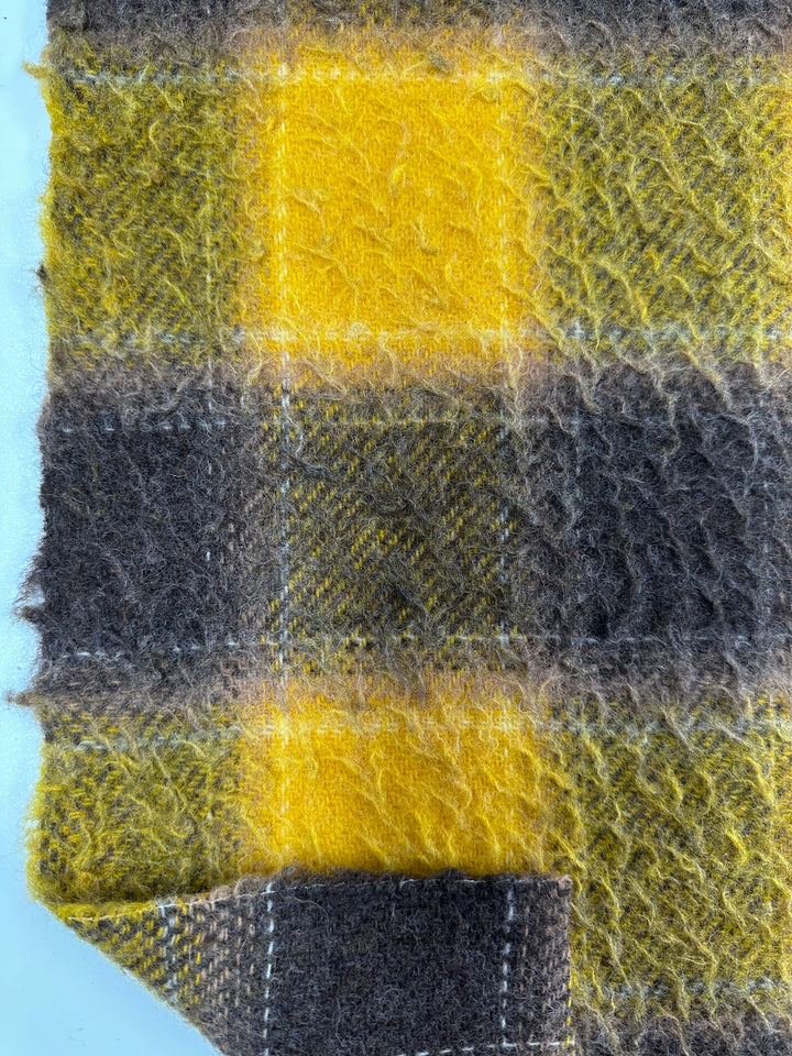 Close-up view of the Virgin Wool - Spruzzo - 145cm by Super Cheap Fabrics. This heavy-weight, fuzzy, and soft wool fabric features a yellow and brown plaid pattern with bright yellow, dark brown, and subtle grayish-green tones. One edge is slightly frayed—ideal for crafting cozy overcoats.