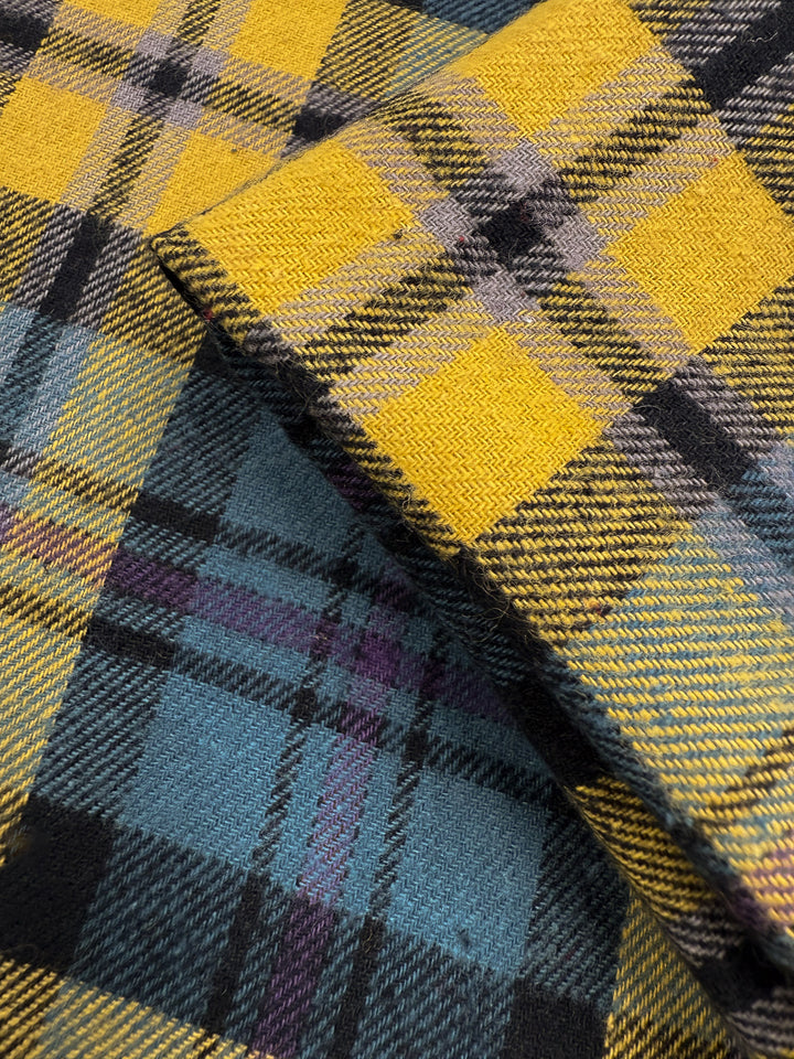 Close-up of two overlapping Flannel Plaid - Highland Dusk fabrics by Super Cheap Fabrics. These medium-weight cotton flannels in yellow, black, grey, and light blue tartan are ideal for shirts. Width: 145cm.