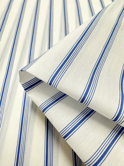 The image showcases a close-up of the GOTS Cotton - Thin Regatta Stripe from Super Cheap Fabrics, featuring a white base with vertically aligned blue stripes. The pattern is crisp and the texture smooth, making it an excellent choice for garment or upholstery projects. Ideal for eco-friendly fashion enthusiasts.