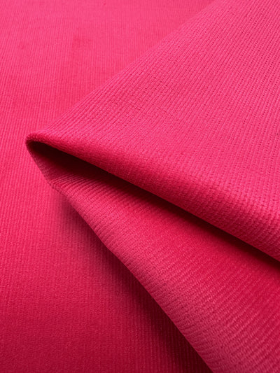 A close-up view of Super Cheap Fabrics' Micro Wale Corduroy in Raspberry Sorbet, folded neatly. The fabric showcases a subtle ribbed pattern that creates a detailed and slightly raised surface. The vibrant raspberry sorbet color is consistent throughout the image, making it ideal for stylish winter clothing or trendy home decor items.