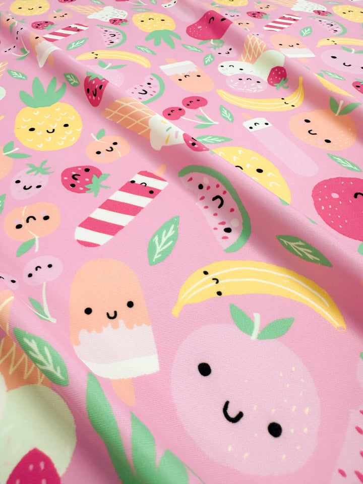 The Printed Nylon Lycra - Fruit Salad from Super Cheap Fabrics is a vibrant pink, soft fabric adorned with playful, high-quality prints of various smiling fruits and treats such as pineapples, bananas, strawberries, watermelon slices, ice cream bars, and popsicles. The cheerful faces add a whimsical touch to this versatile 152cm multiuse design.