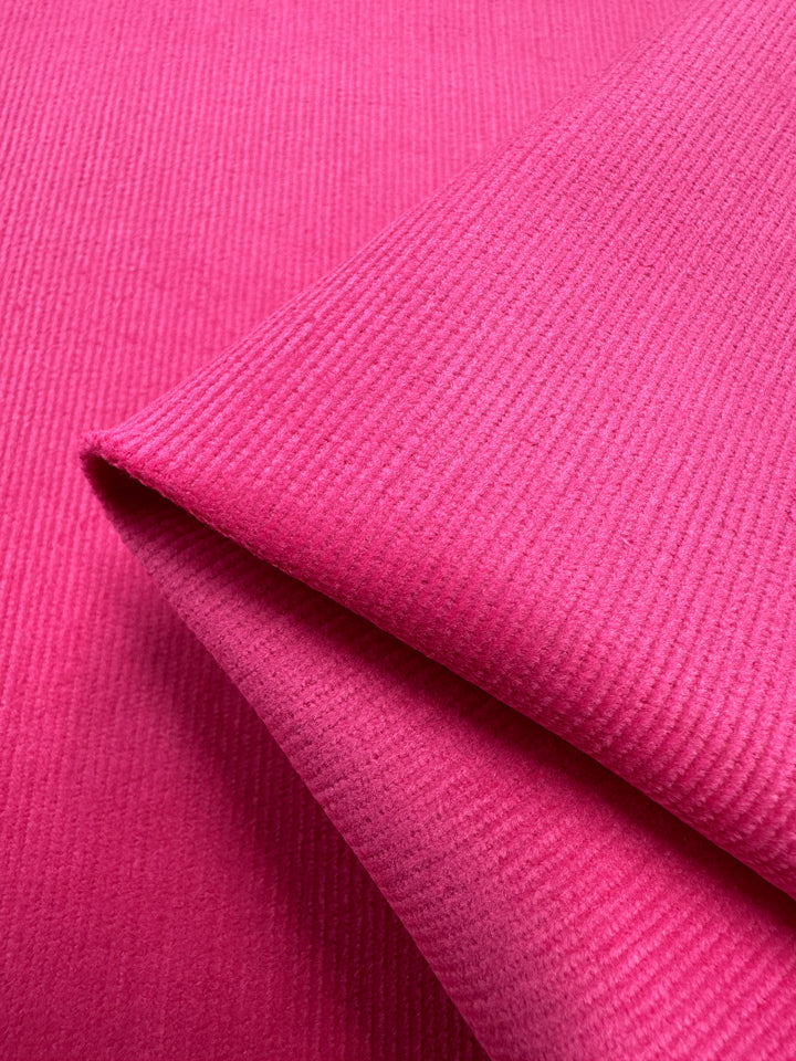 A close-up image of a piece of folded Micro Wale Corduroy in Cabaret from Super Cheap Fabrics. The fabric's distinct ribbed texture is clearly visible, showcasing the soft, velvety material and its vibrant color—perfect for elegant home decor or cozy winter clothing.