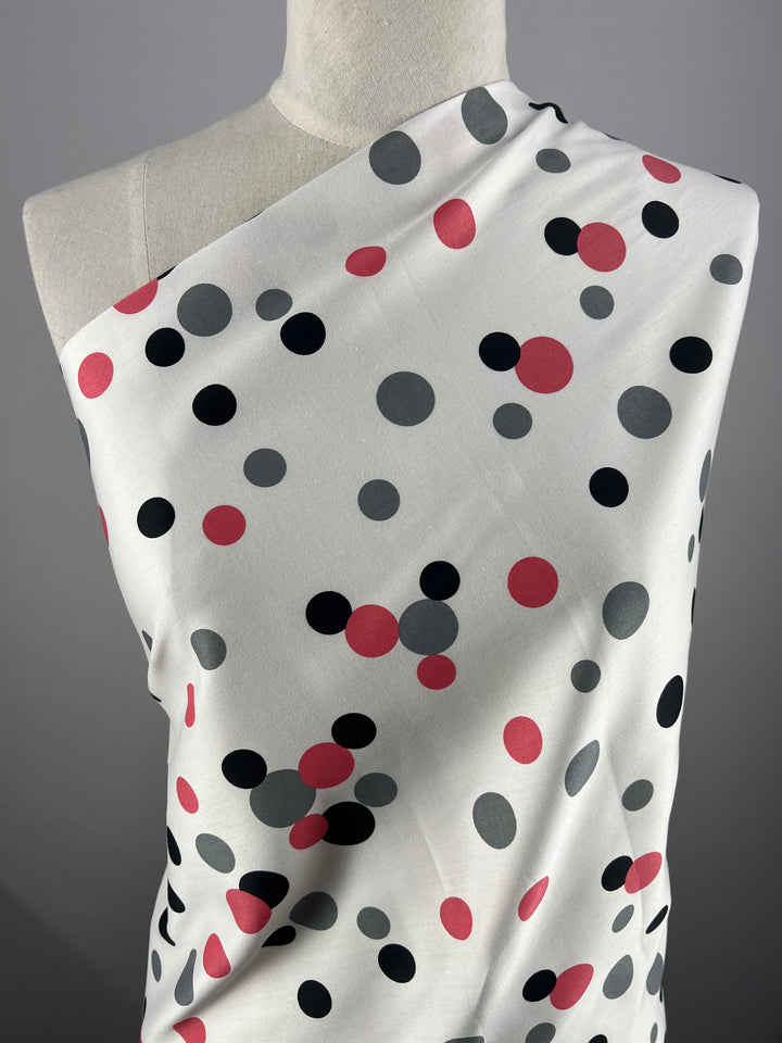 The mannequin is adorned with Super Cheap Fabrics' Cotton Sateen - Bordered Bubbles - 145cm, a lightweight fabric made from 100% cotton. The fabric features a lively pattern of variously sized polka dots in black, grey, and red against a grey background, highlighting its design and texture—perfect for household décor items.