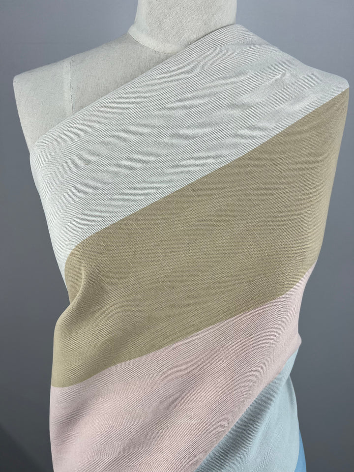 A mannequin displays a sleeveless, one-shoulder garment from Super Cheap Fabrics' Designer Cotton - Blipe - 155cm range, featuring three horizontal color blocks: light grey at the top, beige in the middle, and pale pink at the bottom. Crafted from sustainable deadstock materials, it stands against a plain grey background.