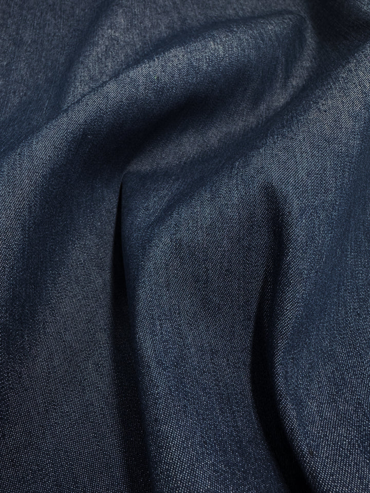 Close-up of Super Cheap Fabrics' Lightweight Denim - Insignia Blue - 150cm, highlighting its soft folds and gentle creases that showcase the texture and weave. The lighting emphasizes the 100% cotton fabric's subtle variations in color and detail.