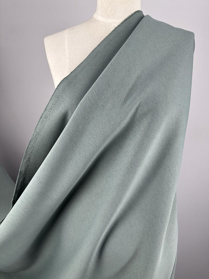 A close-up image of a mannequin draped in Super Cheap Fabrics' Scuba Knit - Mermaid - 165cm. The light grey material appears to be smooth and flowing, wrapping around the shoulder and chest area of the mannequin against a neutral background.