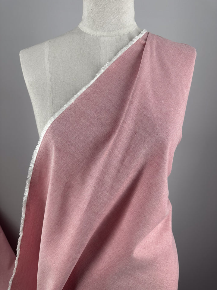 Super Cheap Fabrics' Oxford Cotton - Confetti - 146cm, a light pink fabric with a white frayed edge, is draped diagonally over a dress form against a plain gray background.