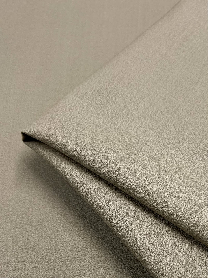 A close-up image of a neatly folded piece of the Merino Wool Suiting in Oxford Tan, featuring a smooth texture. The fabric's fine weave and soft sheen, indicative of luxurious texture, reveal its high-quality material from Super Cheap Fabrics. Additionally, the excellent breathability and perfectly aligned edges showcase a clean and precise fold.