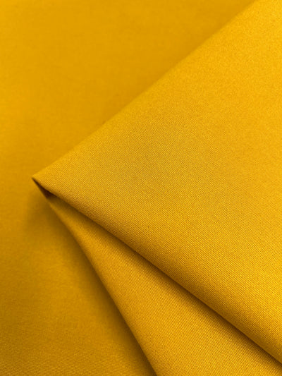 A close-up of a folded piece of Milano Ponte - Symphonic Sunset fabric from Super Cheap Fabrics, highlighting its bright yellow, heavy-weight material with a smooth texture and even surface. The gentle reflection of light off the fabric accentuates its rich, vibrant color—a true symphonic sunset.