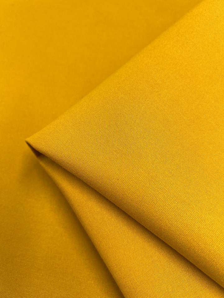 A close-up of a folded piece of Milano Ponte - Symphonic Sunset fabric from Super Cheap Fabrics, highlighting its bright yellow, heavy-weight material with a smooth texture and even surface. The gentle reflection of light off the fabric accentuates its rich, vibrant color—a true symphonic sunset.