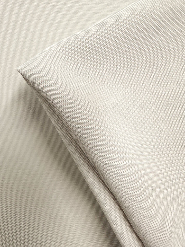 A close-up photo showcases Super Cheap Fabrics' Suiting - White Swan (142cm), featuring softly folded beige polyester on a flat background to highlight the subtle texture and fine weave of this medium weight fabric.