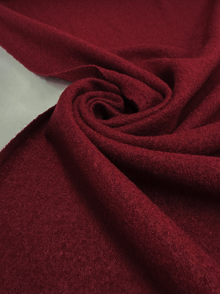 Close-up of Super Cheap Fabrics’ Boiled Wool - Rhubarb (145cm), deep red in color, partially rolled and folded to display its soft, slightly textured surface.