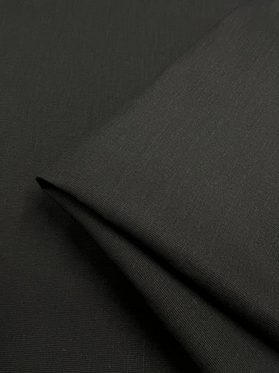 A close-up shot of smooth, black twill *Suiting - Black - 150cm* from *Super Cheap Fabrics* folded over itself. The material appears to have a subtle, fine texture and is neatly arranged, highlighting its seamless and sleek finish. This versatile fabric exudes elegance with its lightweight drape.