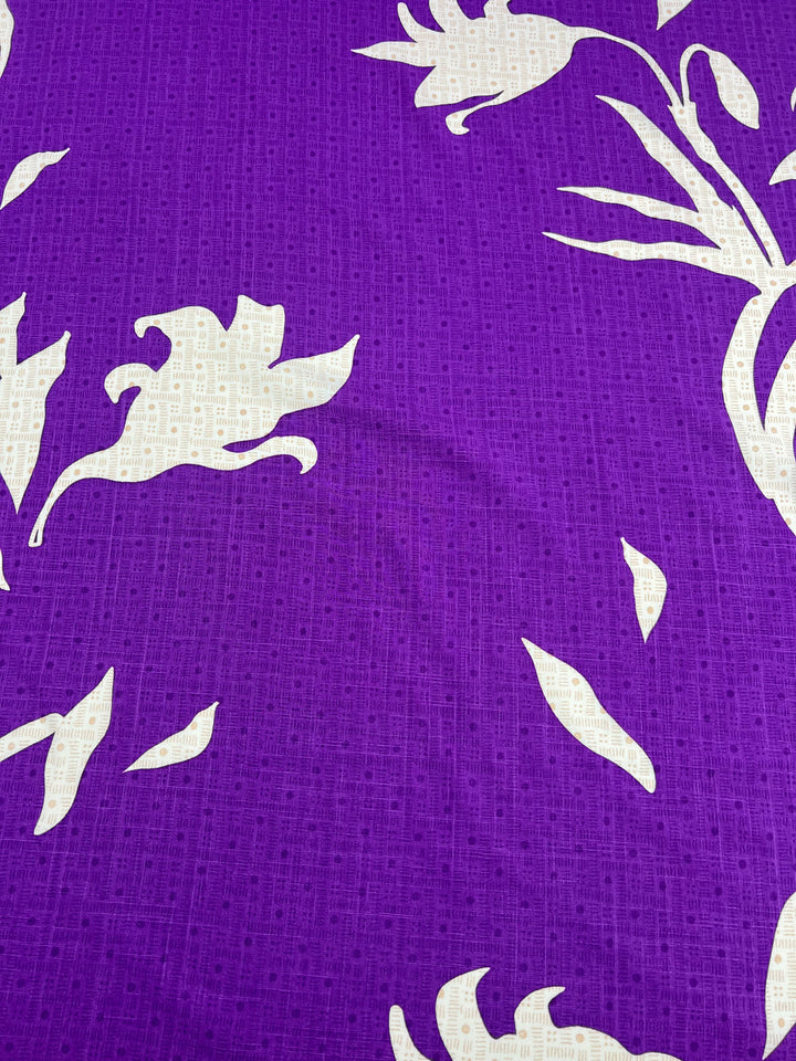 A close-up image of the Super Cheap Fabrics product, Bamboo Rayon - Lily Shadows - 152cm, showcasing its lightweight fabric with a vibrant purple background adorned with large white flowers, leaves, and stems. The design offers a bold and striking contrast against the purple Bamboo Rayon fabric, making it ideal for beginner-friendly projects.