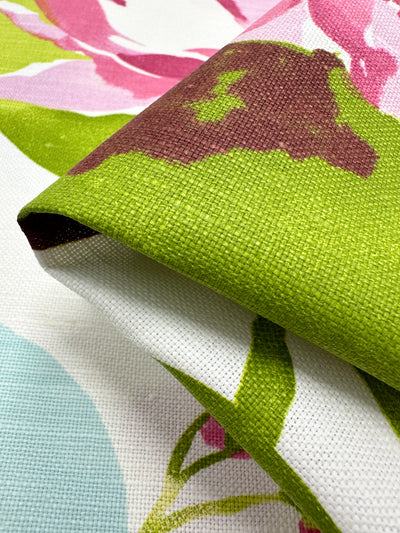 Close-up of a colorful Blended Duck - Tambala fabric swatch showcasing a floral pattern. The design features green, pink, and brown hues on a textured Linen Cotton Fabric surface. Perfect for home décor accessories, the fabric's folded details reveal its vibrant colors and intricate weave. Brought to you by Super Cheap Fabrics, this material spans 150cm in width.