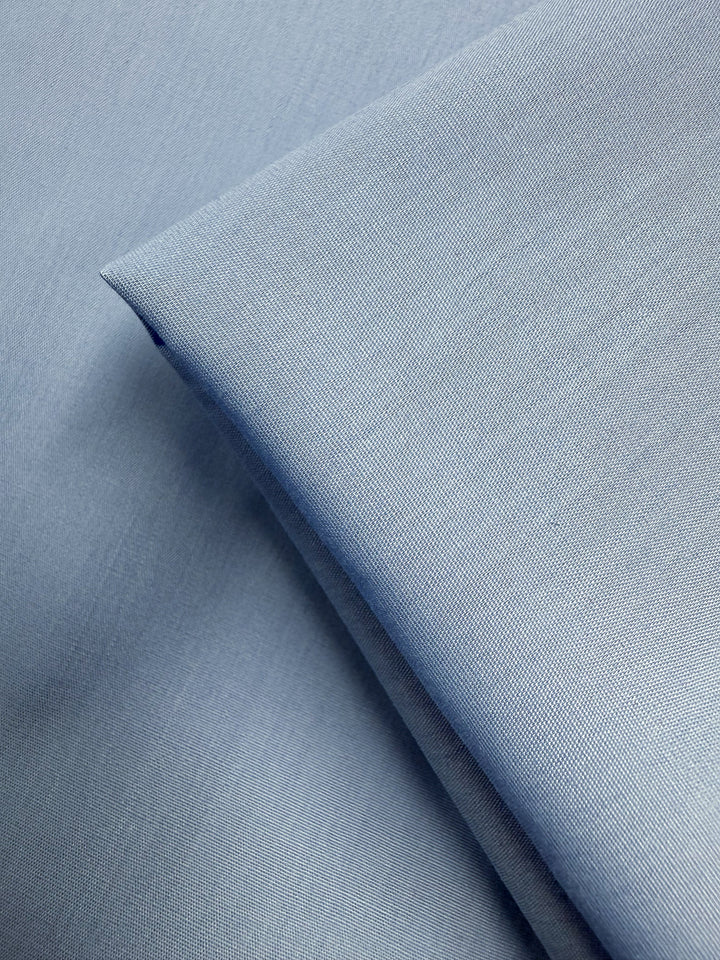 Close-up of Super Cheap Fabrics’ Poplin - Powder Blue - 114cm, a lightweight poly cotton fabric with a smooth texture and fine woven details, shown neatly folded and layered.