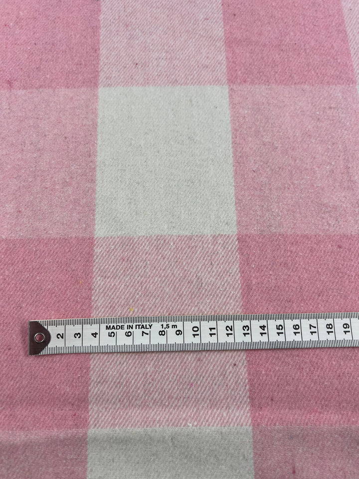 A piece of the Flannel Plaid - Tickled Pink fabric from Super Cheap Fabrics is laid flat, with a measuring tape in centimeters placed horizontally across it. The tape measure reads "MADE IN ITALY" and shows up to 13 centimeters in view.