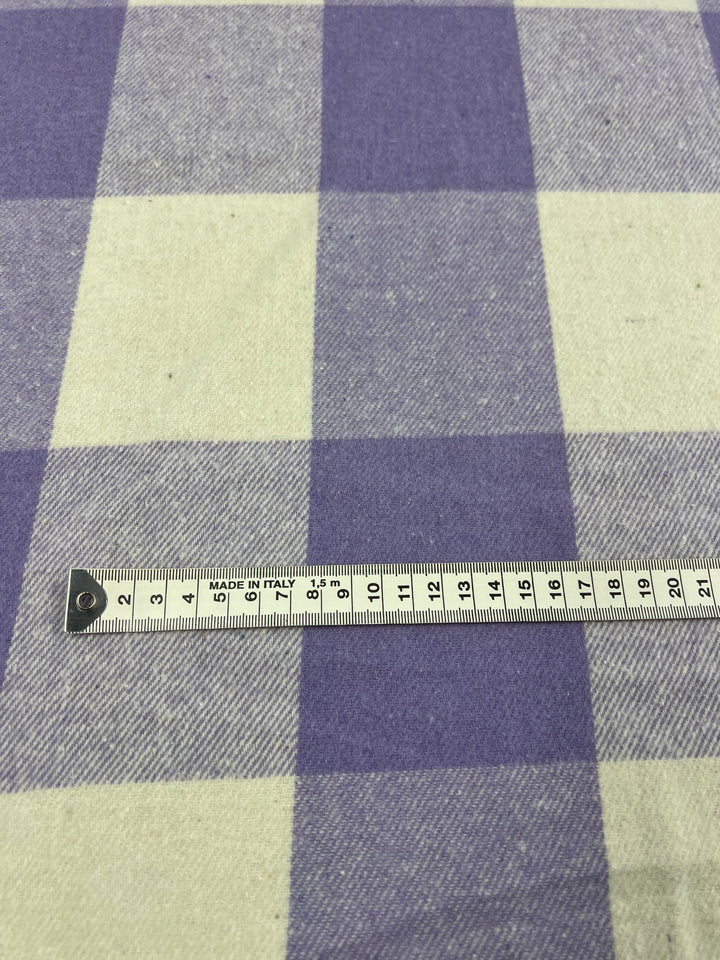 A close-up of the Flannel Plaid - Viola - 148cm fabric by Super Cheap Fabrics, showcasing its durable polyester material with a charming viola and off-white checkered pattern. A measuring tape is stretched out horizontally across the fabric, displaying measurements from 0 to 20 centimeters.