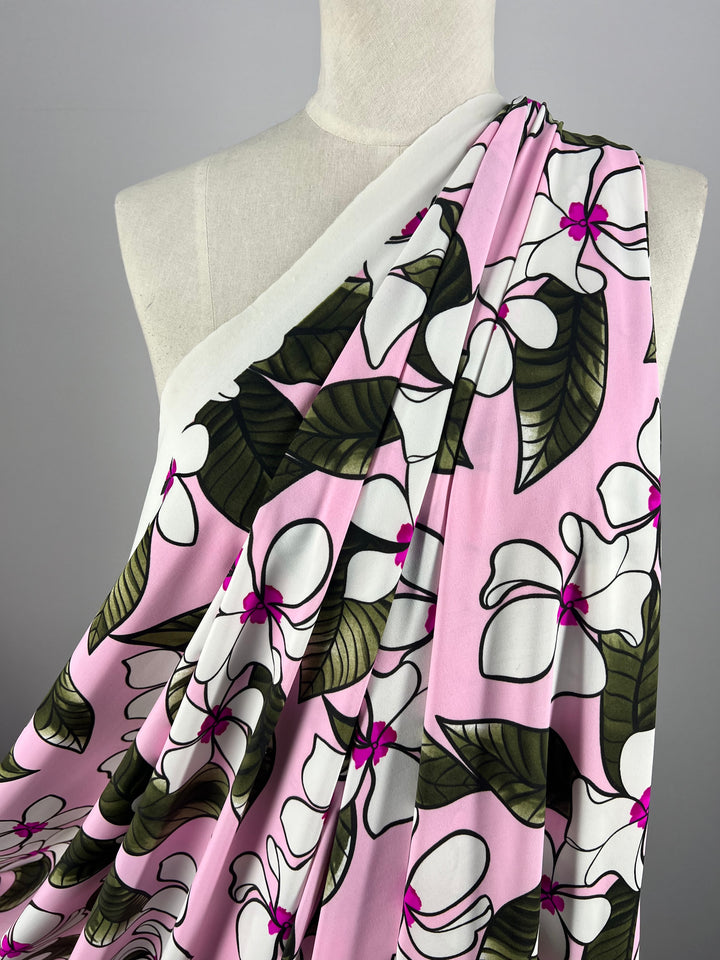 A mannequin displays a draped piece of light to medium weight Printed Nylon Lycra - Paraplu - 145cm fabric by Super Cheap Fabrics, featuring a floral pattern. The fabric has a light pink background with large white flowers, green leaves, and small magenta accents. The multiuse arrangement showcases the fabric's high-quality print and texture.