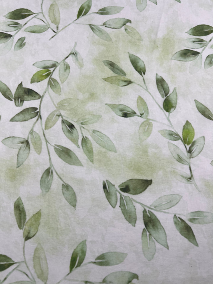 This elegant fabric pattern, known as Designer Cotton - EUCAS - 150cm from Super Cheap Fabrics, features green watercolor leaves on a light, slightly textured background. The leafy branches are scattered across the lightweight cotton fabric, creating a natural and peaceful theme perfect for luxury sewing projects.