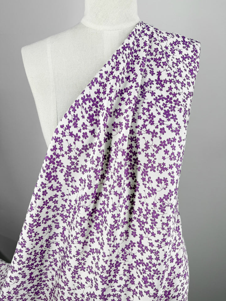 Super Cheap Fabrics’ Mercerised Rayon - Violet Meadow (150cm) features a lightweight, breathable fabric with densely packed purple floral patterns, draped over a white dress form and set against a plain gray background.