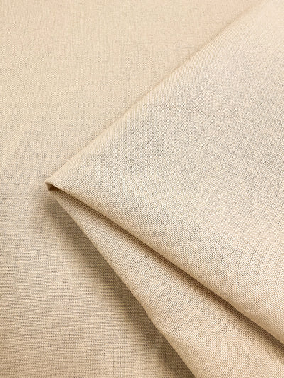 A piece of the Premium Linen Cotton - Shortbread from Super Cheap Fabrics, measuring 140cm and featuring a lightweight design with a subtle woven texture, is neatly folded at the corner to create a layered appearance.