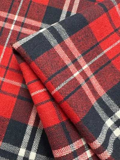 Close-up of the Super Cheap Fabrics Suiting - Trad Tartan - 147cm, showcasing its lightweight fabric with a red, black, and white plaid pattern. The intersecting lines form a classic tartan design with a mix of thick and thin stripes, giving it a textured appearance. Ideal for twill suiting, the fabric looks soft and slightly textured.