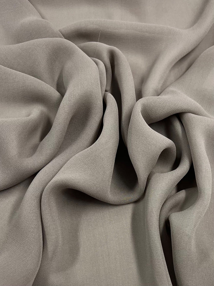 Close-up of a smooth, flowing Silk Georgette - Earth fabric from Super Cheap Fabrics with soft folds and creases. The lightweight 135cm fabric's texture is highlighted by the light and shadows, giving it a luxurious and elegant appearance—perfect for spring and summer outfits.