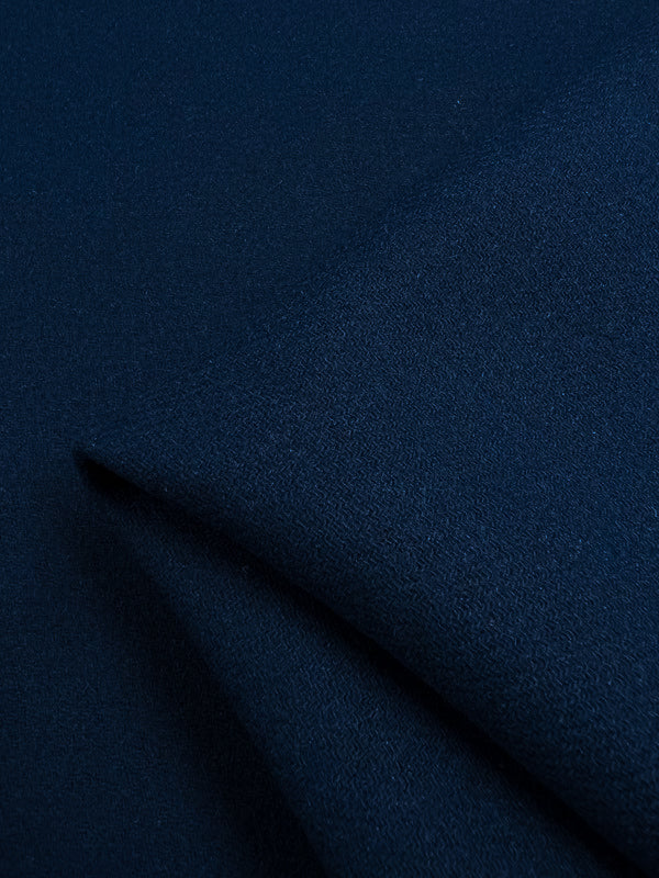 A close-up view of the "Wool Cashmere - Navy Peony - 150cm" from Super Cheap Fabrics showcases its smooth and even texture. This fabric, reminiscent of extra heavy weight wool, is slightly folded in the bottom left corner, allowing light to highlight its soft and uniform surface.