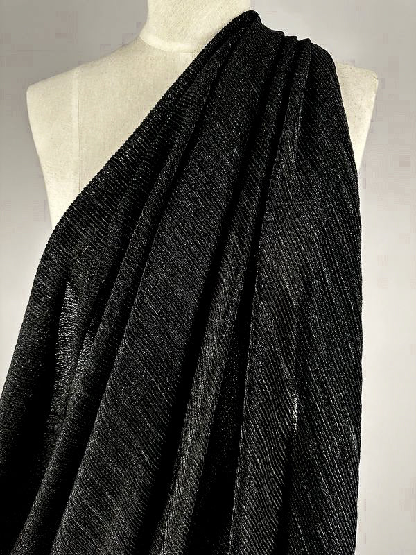 A black Metallic Knit from Super Cheap Fabrics, measuring 150cm, draped over a white dress form. The medium to heavy weight fabric has a subtle sheen and appears to be of substantial weight. The pleats add texture and dimension to the cloth as it cascades down the form, ideal for sophisticated dresses.