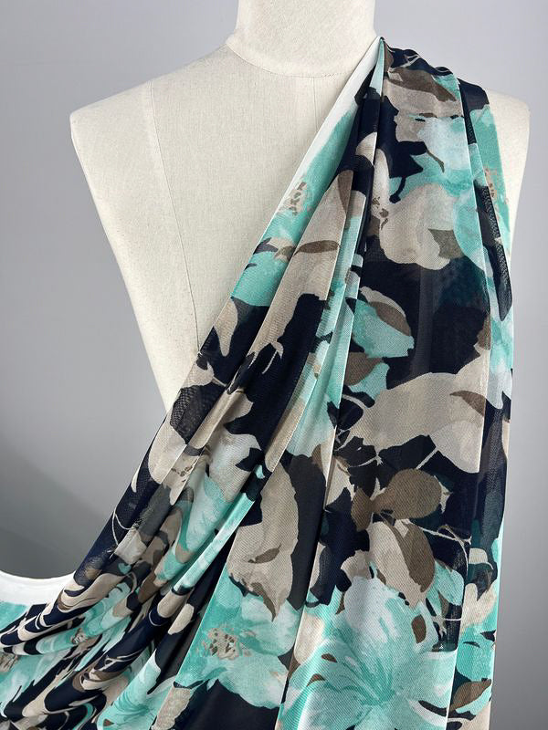 A close-up photo of a white mannequin draped with Super Cheap Fabrics' Printed Mesh - Lilly - 145cm, showcasing its vibrant and elegant floral pattern. The fabric features a mix of blue, black, and beige colors, making it perfect for whimsical home decor. The plain and neutral background highlights the exquisite design of the fabric.